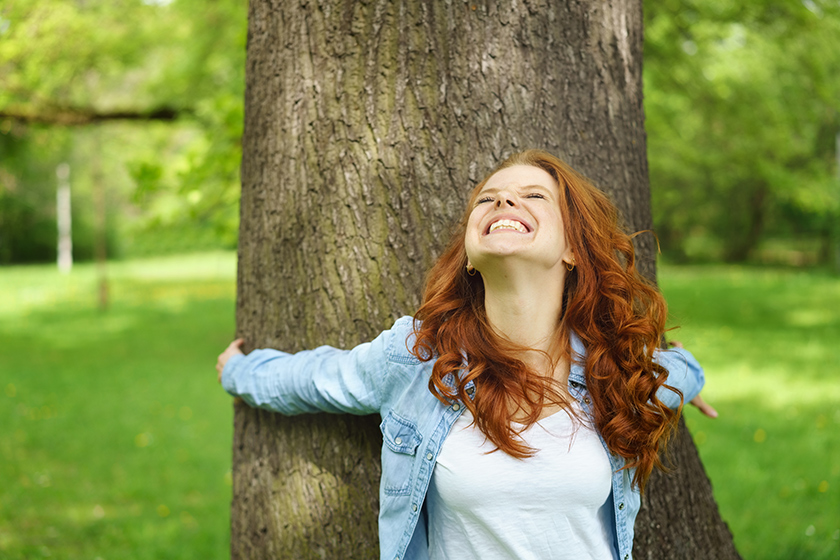 Eine Frau umarmt glücklich einen Baum im Wald.